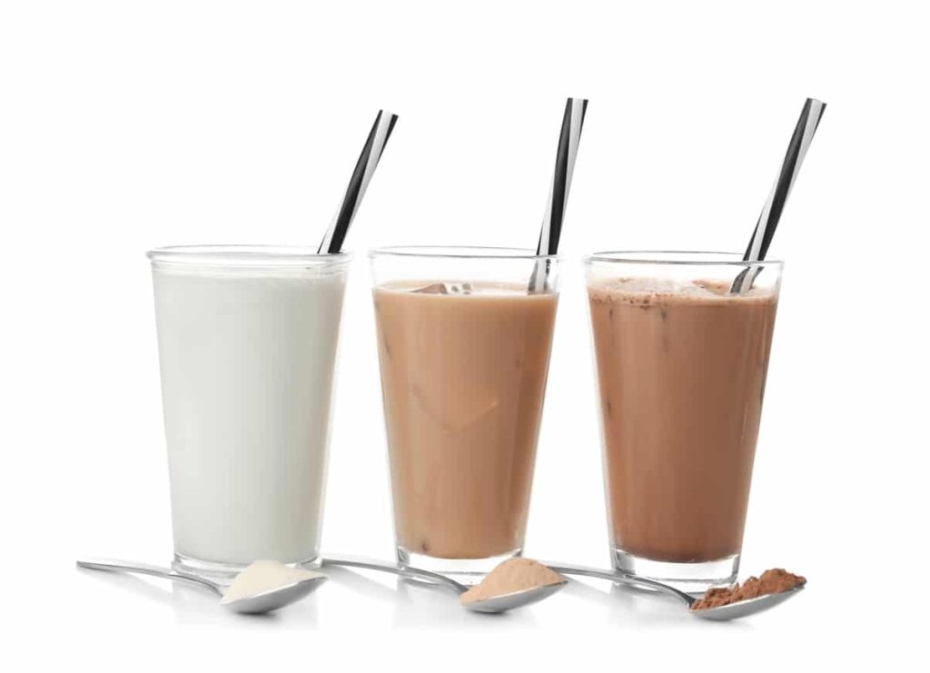 Glasses with different protein shakes and powders in spoons on white background